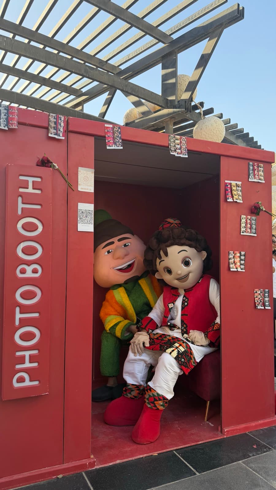 Two costumed mascots sitting inside the red photo booth at Bazarna Society