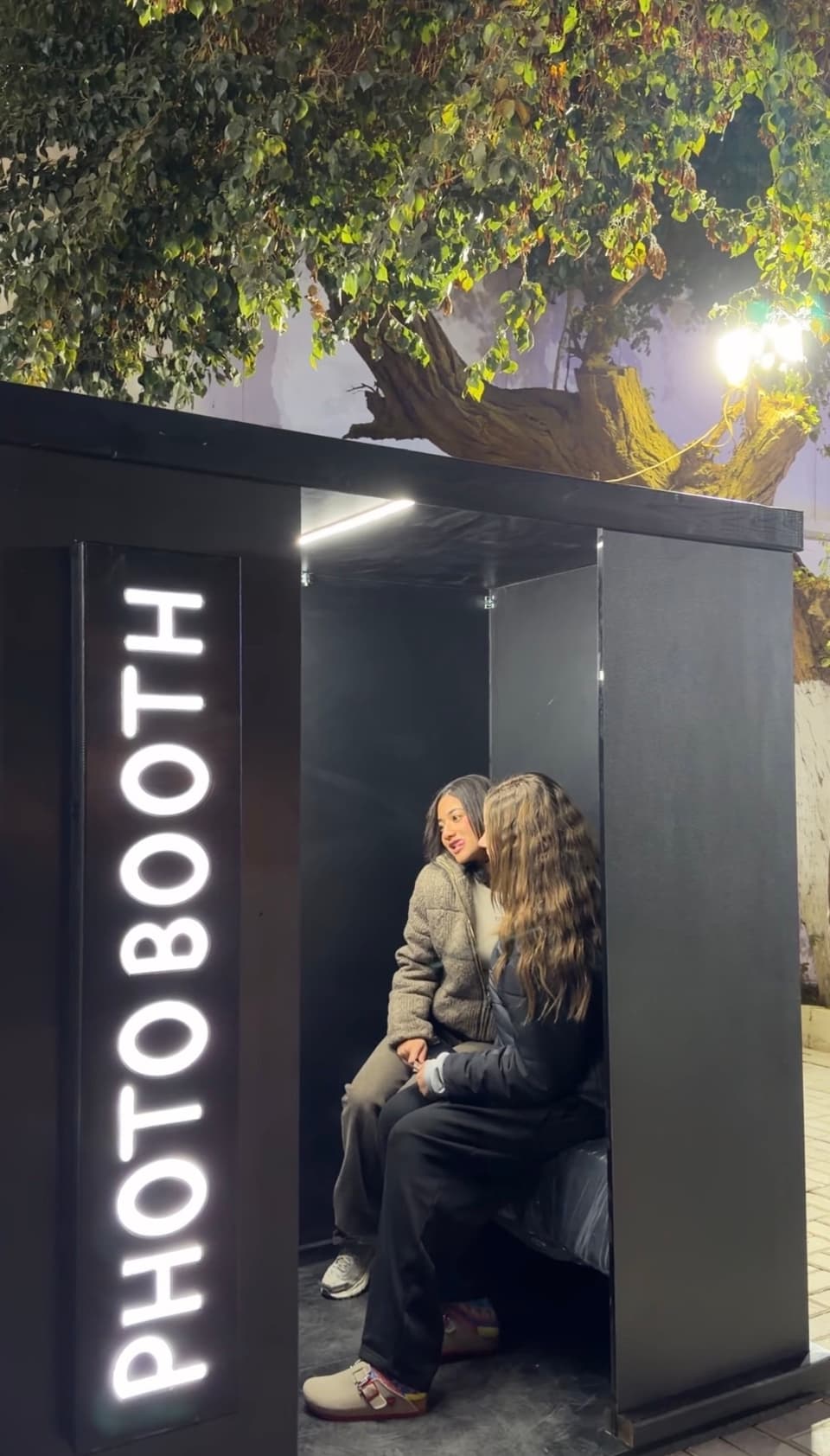 Guests posing inside the black enclosed photo booth under the trees at The Field